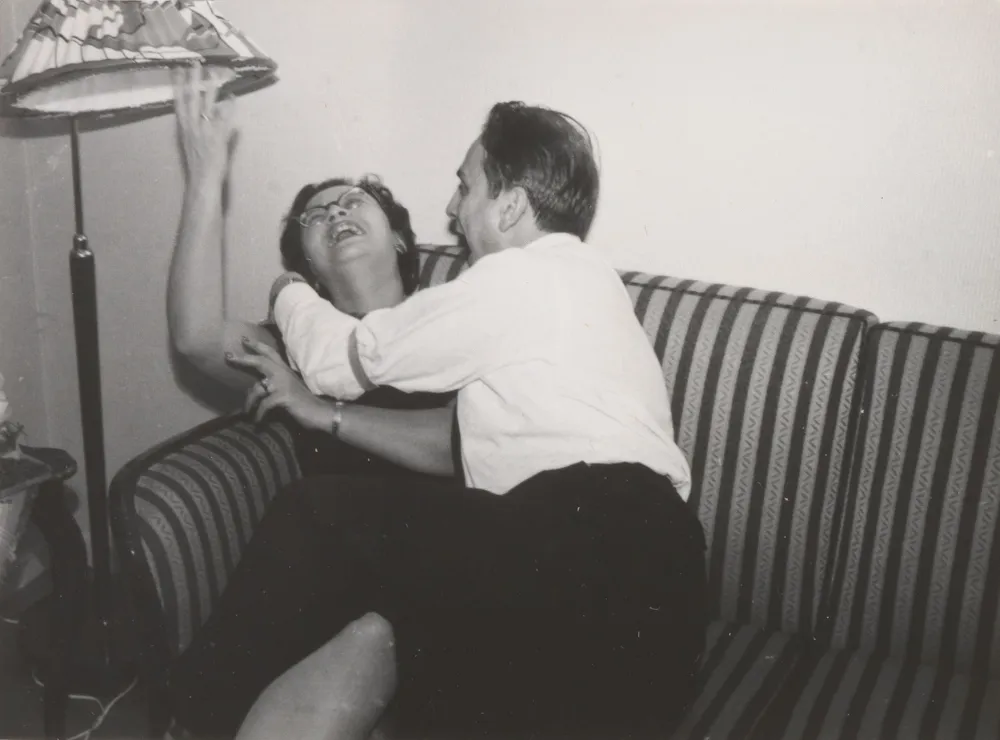 A woman and a man joke on a striped sofa under a lampshade.