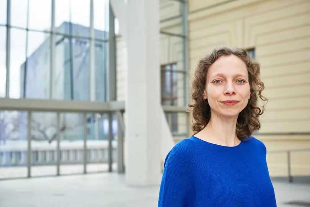 Portrait photo of a smiling woman wearing a bright blue jumper: she looks directly into the camera.