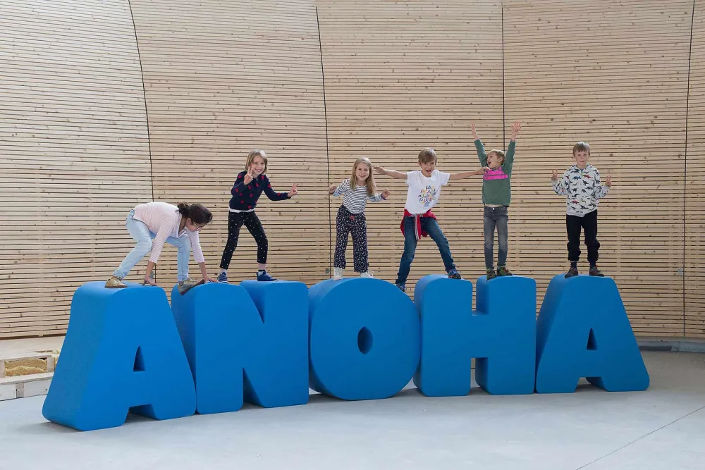 Children perform on life-size letters, which form the lettering ANOHA