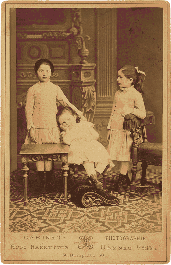 Historical black and white photograph of three children in white dresses.