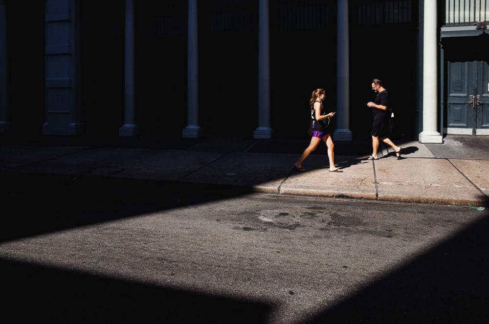 On a sidewalk, two people looking at their smartphones walk towards each other.