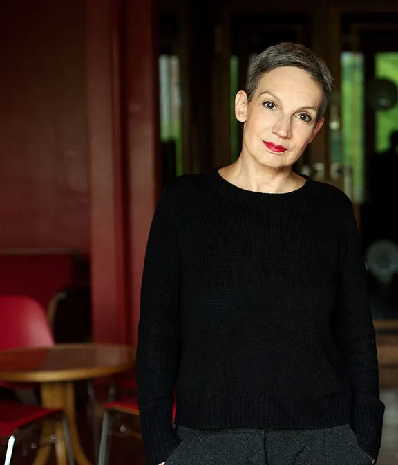 Portrait of Marion Brasch, hands in pockets, with bar table in the background