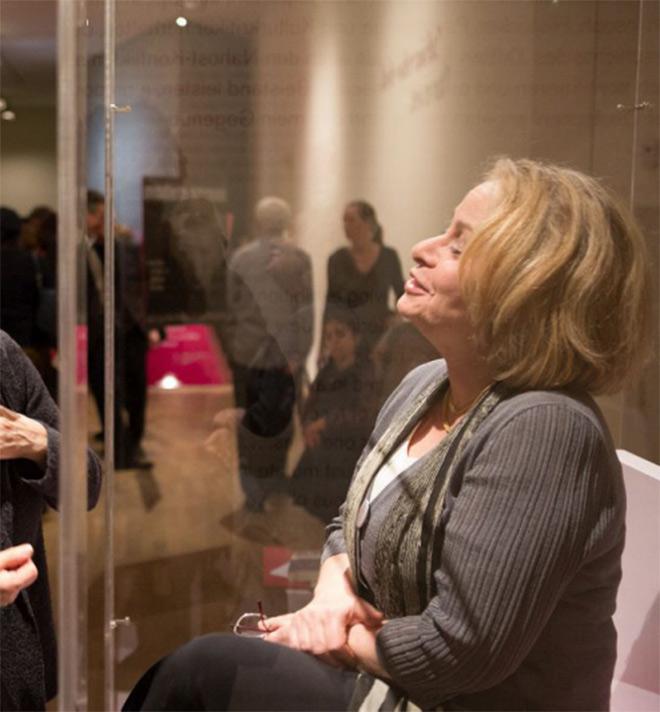 A woman behind glass, in the background visitors of the exhibition