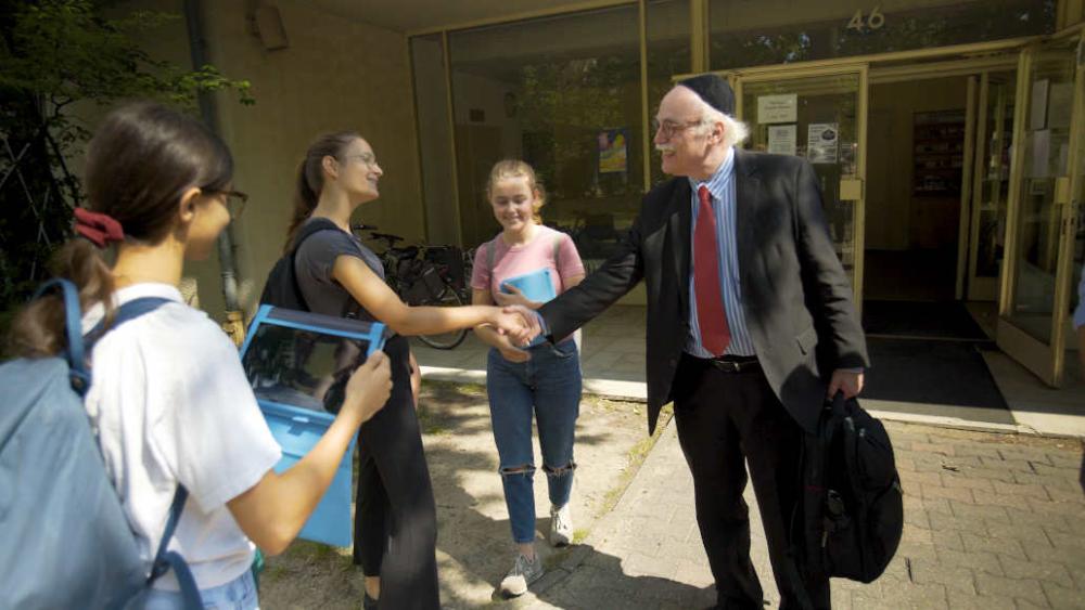 Rabbiner Professor Andreas Nachame steht mit Jugendlichen vor einem Hauseingang und schüttelt einem Jugendlichen die Hand.