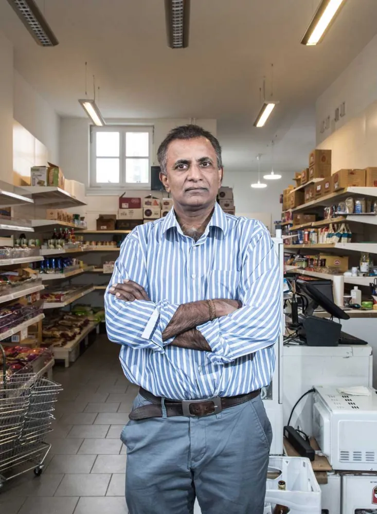 A man in a striped shirt is standing with his arms crossed in a grocery store.
