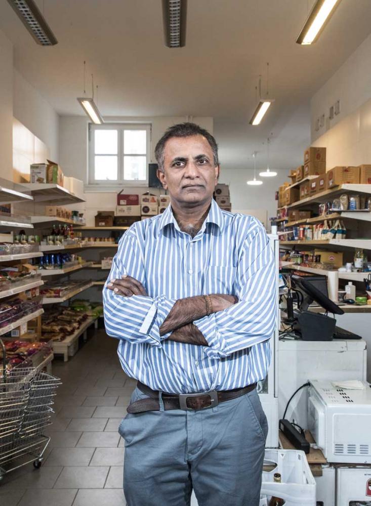 A man in a striped shirt is standing with his arms crossed in a grocery store.