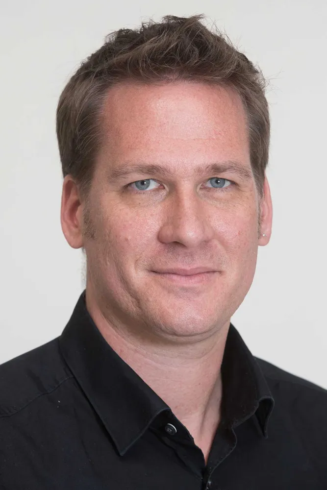Portrait of a man with short medium-blond hair and a black shirt, smiling at the camera.