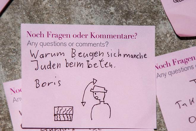 Ein pinker Post-it-Zettel beschriftet mit „Warum Beugen sich manche Juden beim beten?“