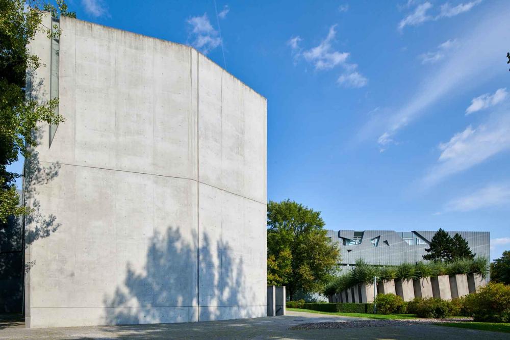 A concrete tower, in the background a new building made of metal elements.