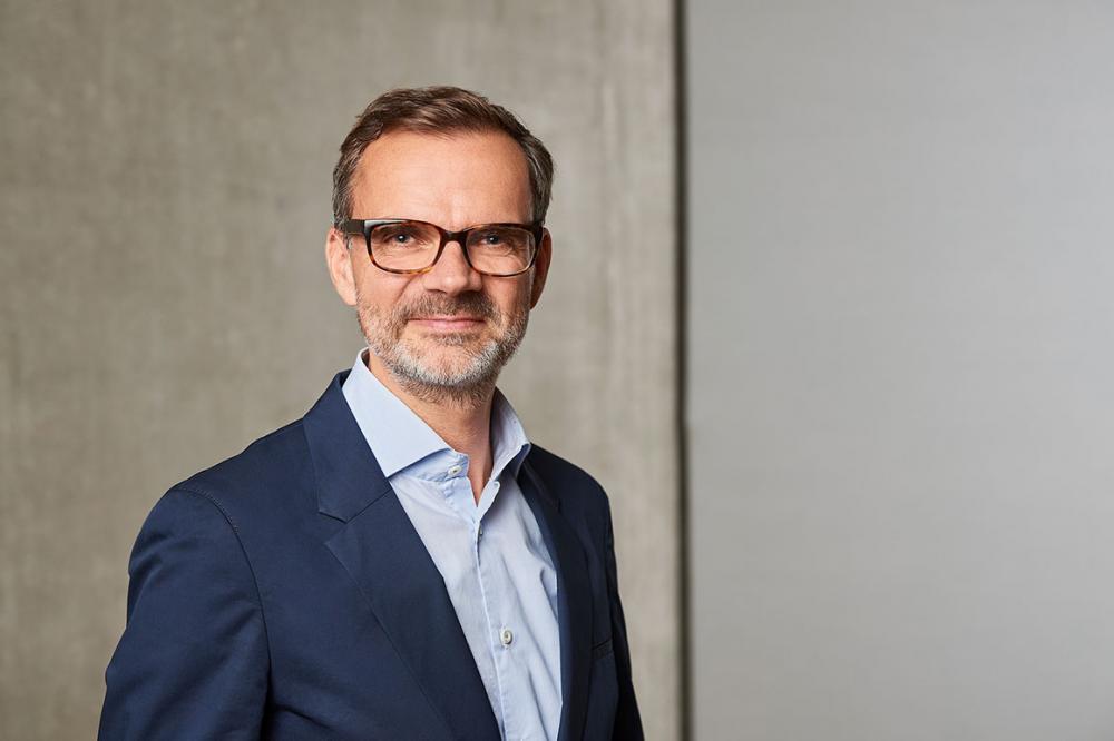 Portrait of a man with glasses, beard, dark blue jacket and light blue shirt.