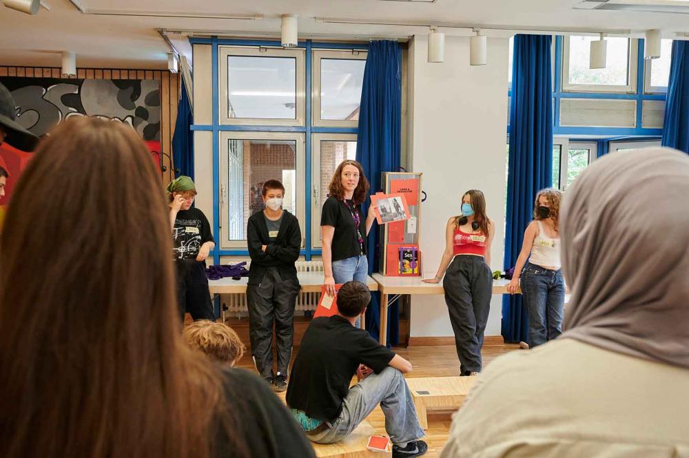 Young people look at a woman holding up a red card with a photograph.