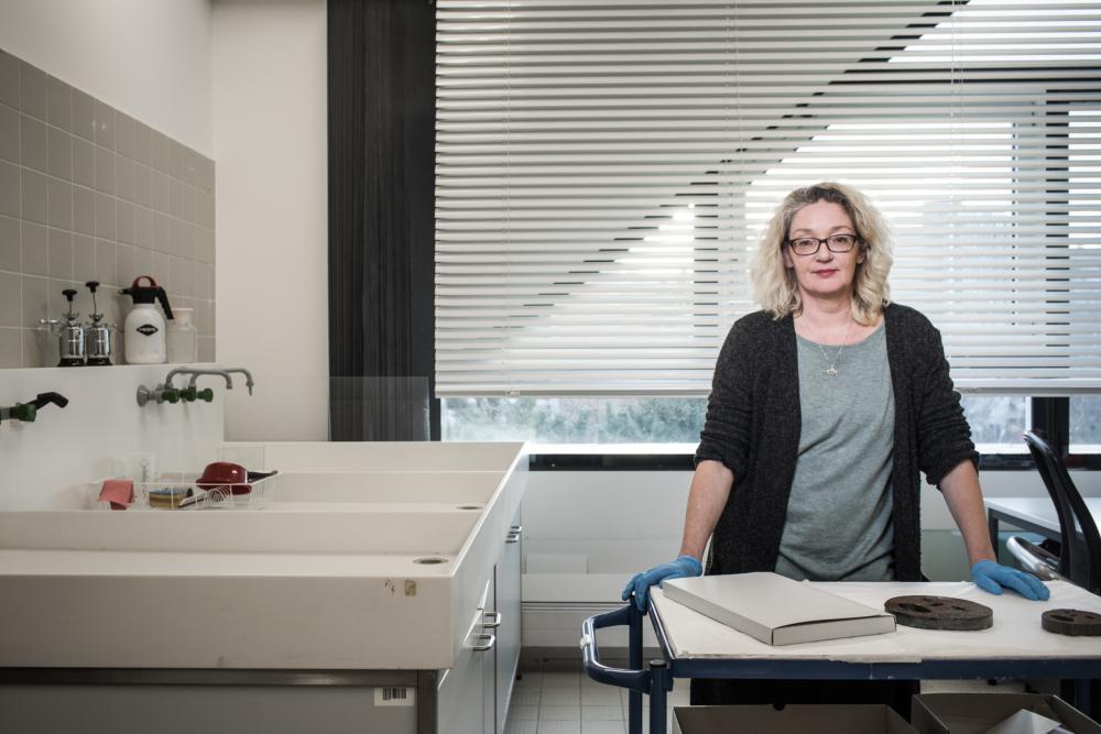 A woman with blue rubber gloves standing at a desk with various objects on it.