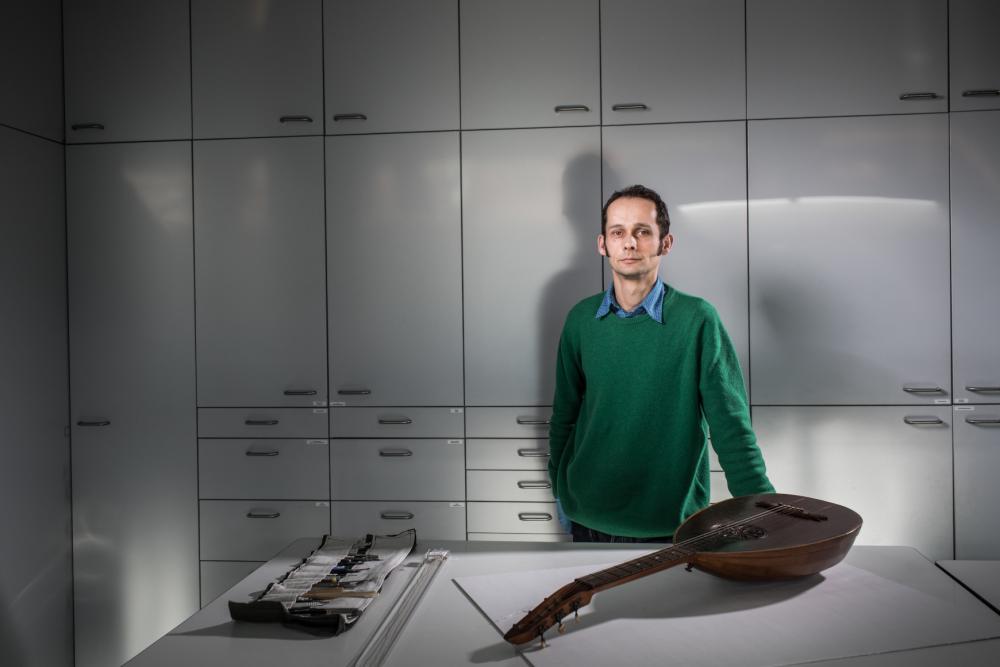 A man standing at a desk, in front of him lies an old wooden instrument