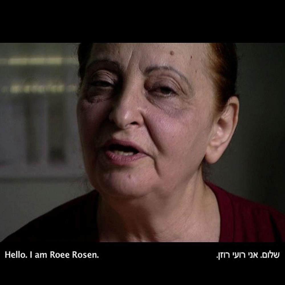 Screenshot with the face of a speaking woman, at the bottom of the screen it says in English and Hebrew: “Hello, I am Roee Rosen.”