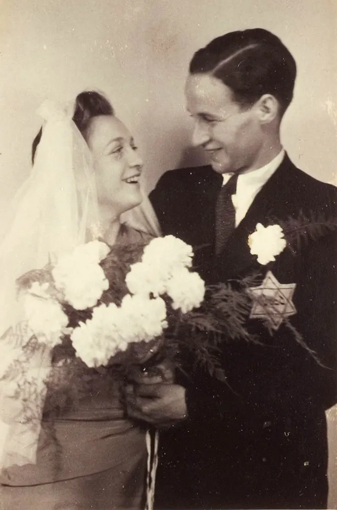 Black and white photograph of a couple with a bouquet of flowers and a veil, a yellow badge on his jacket.