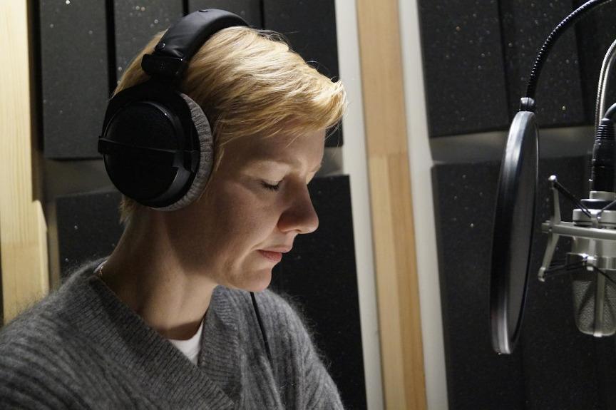 The actress and speaker Sandra Hüller sits with headphones in front of the microphone in the recording studio