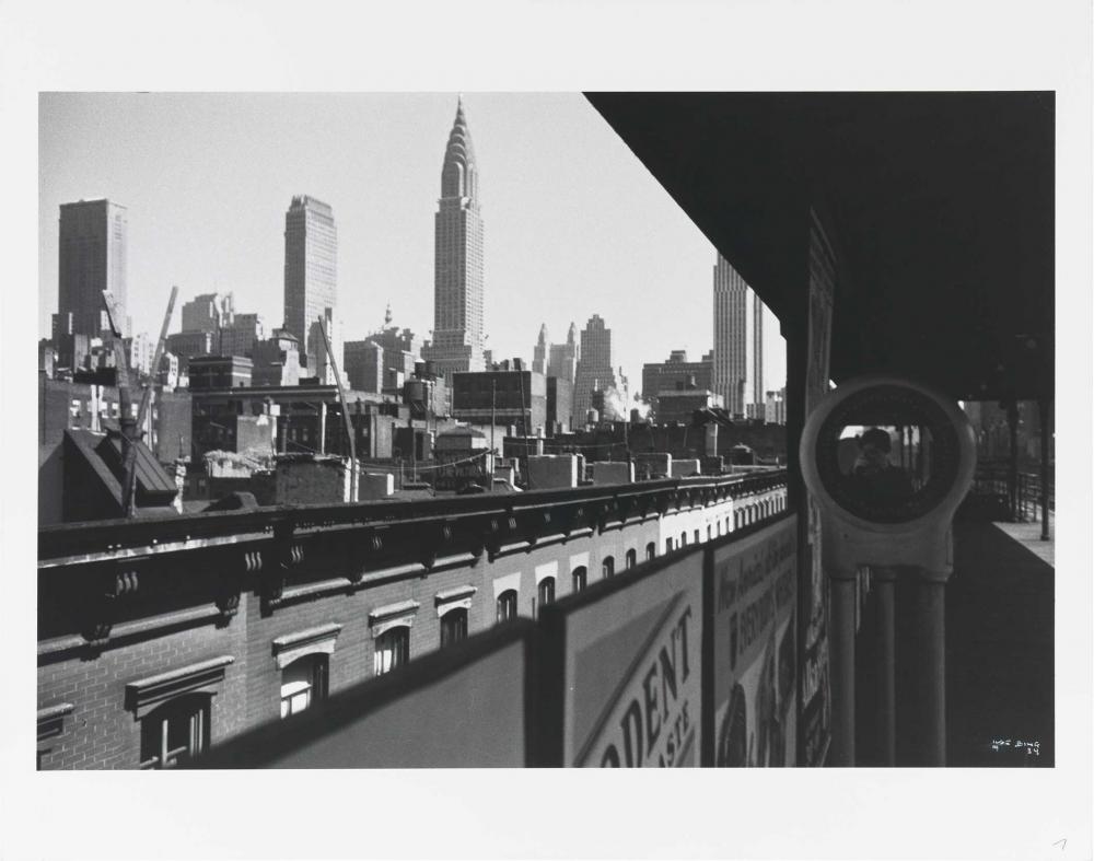 Houses and skyscrapers, a platform, on it a mirror in which the photographer can be seen with her camera.