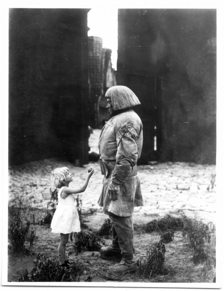 Filmstill from the movie “The Golem, How He Came Into the World” by Paul Wegener:A child in a white dress hands an apple to the Golem.