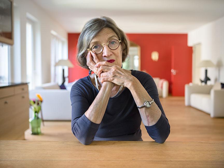 A woman sits at a table with her chin resting on her hands, in the background a spacious living room