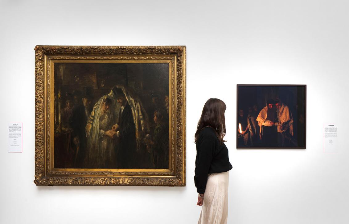 Exhibition view, a woman stands in front of a wall on which a painting hangs on the left and a photograph on the right.
