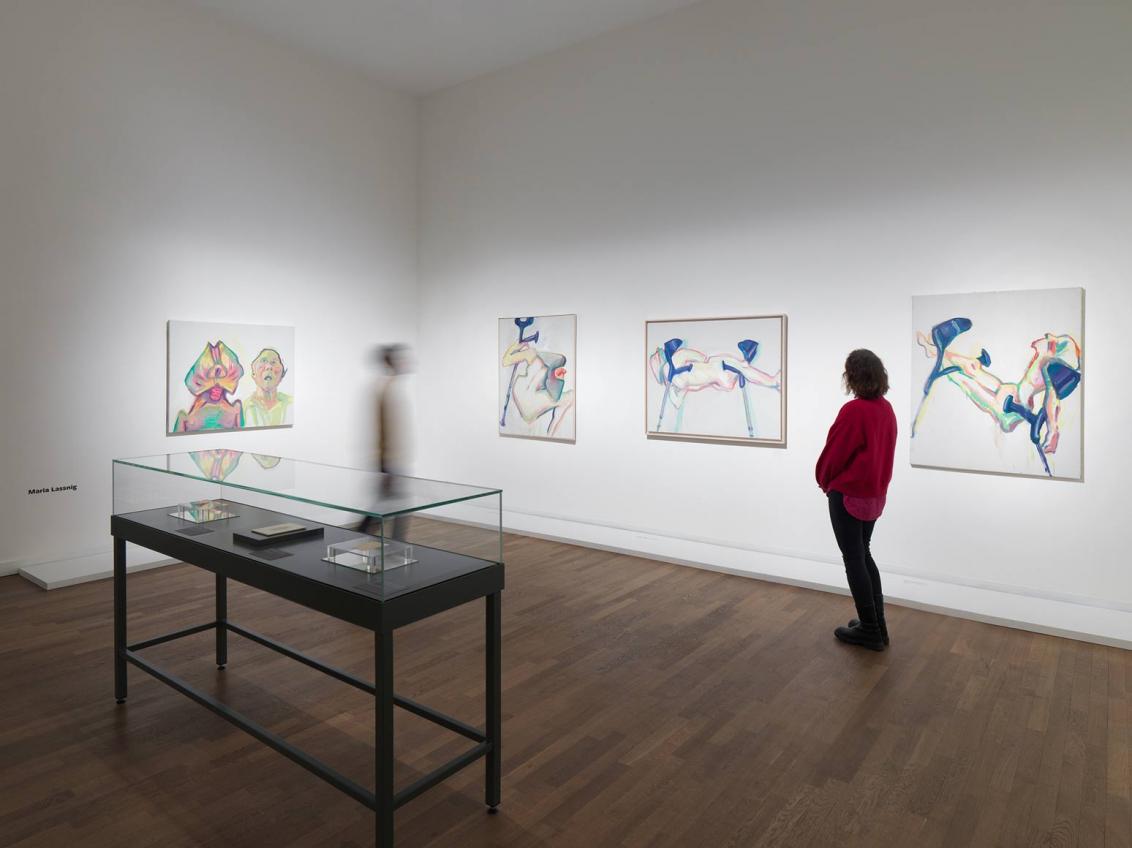 Person with a red sweater looks at paintings on the walls of an exhibition room.