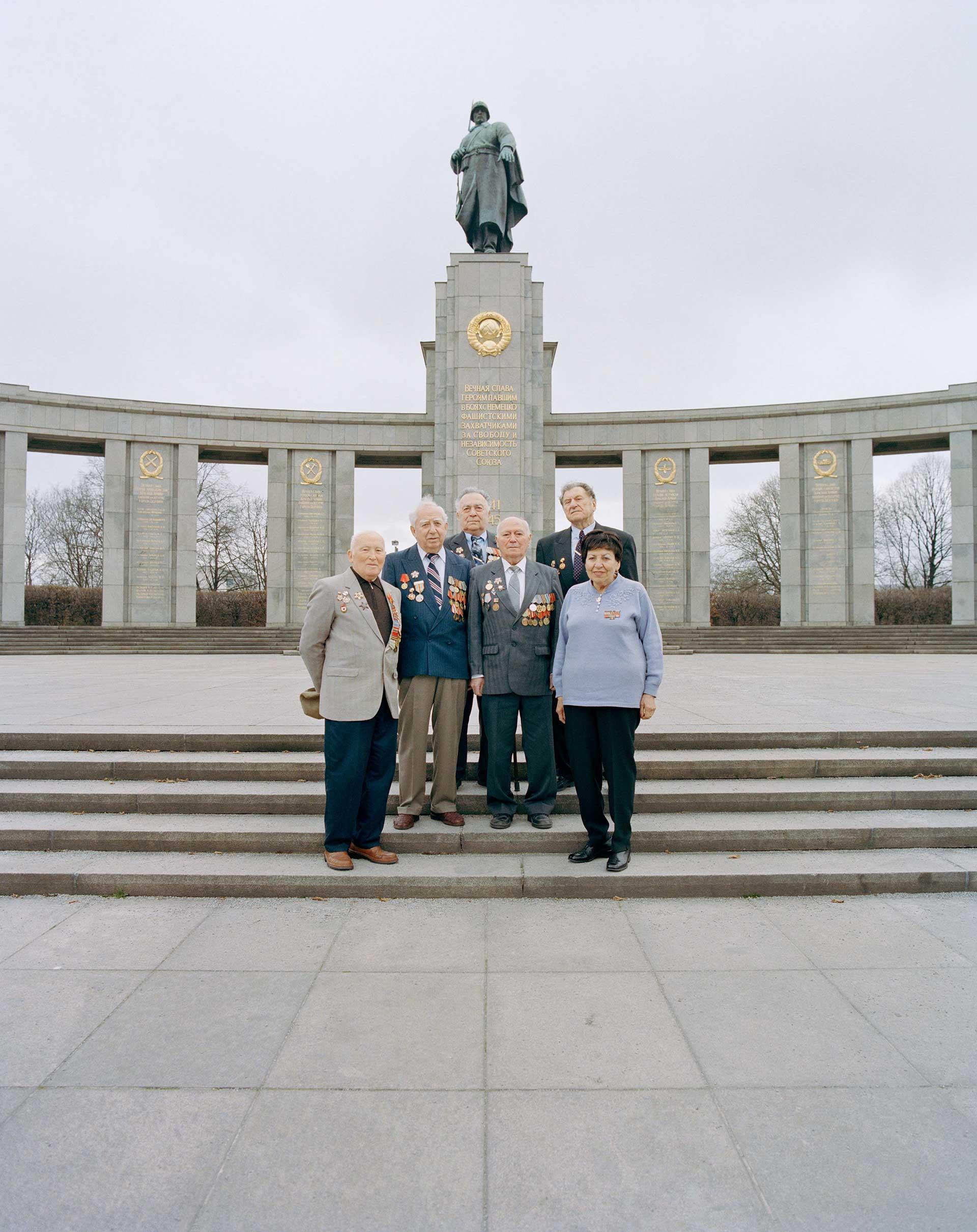 Old people stand on the steps in front of a monument.