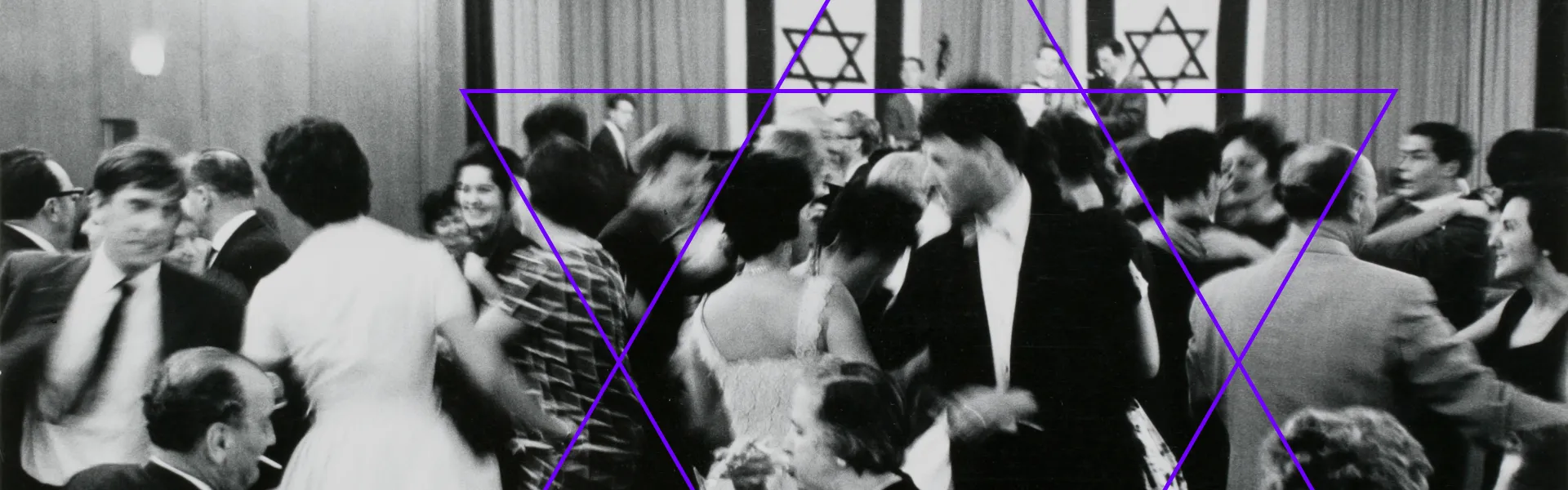 Schwarzweiß-Fotografie: Festlich gekleidete Menschen beim Tanzen, im Hintergrund ist eine mit zwei israelischen Fahnen geschmückte Bühne zu sehen, auf der eine Musikkapelle spielt.