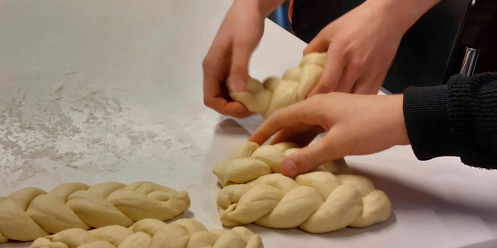 Hands make plaits of dough on a table.