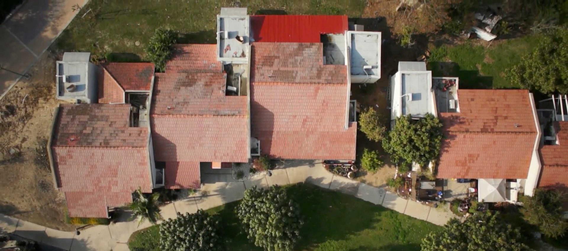 Bird’s eye view of several row houses with red roofs. They are surrounded by trees, front gardens and driveways.