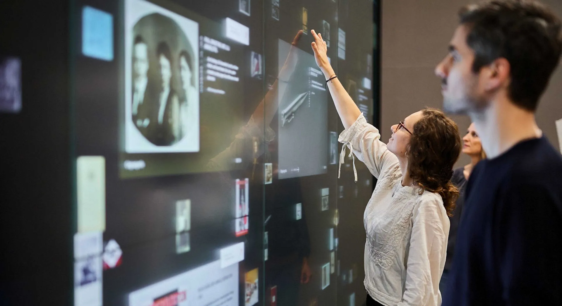 People touch a large touchscreen wall that displays documents and objects