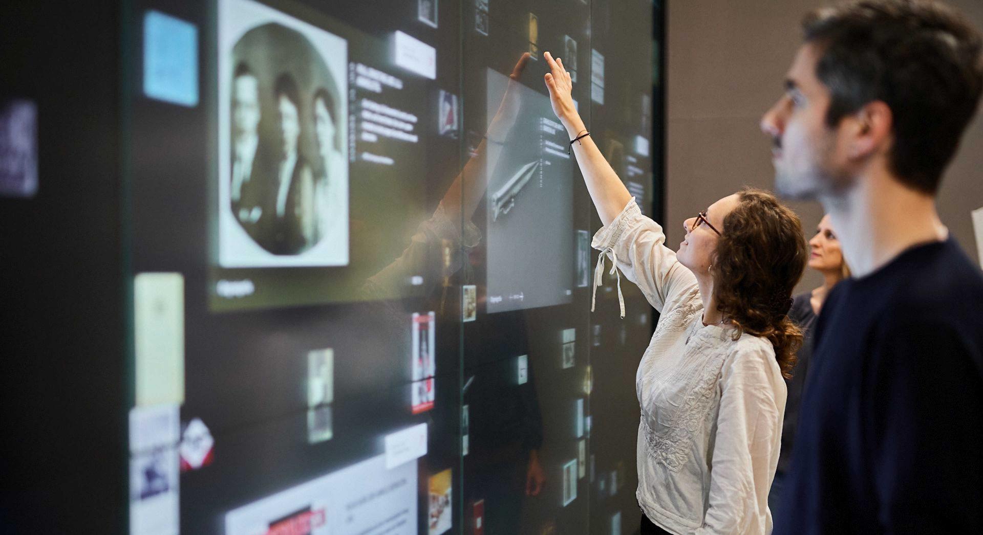 People touch a large touchscreen wall that displays documents and objects