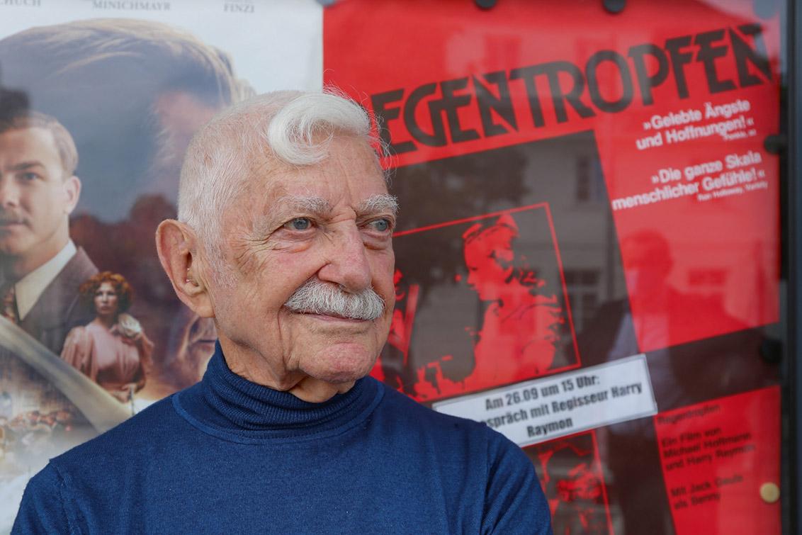 Portrait of Harry Raymon with film poster in the background