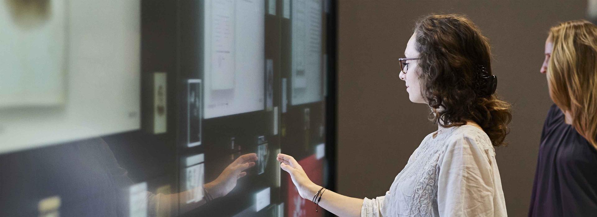 Several people stand in front of a digital wall on which documents and photos are displayed. One of the people touches the media installation to interact with it.