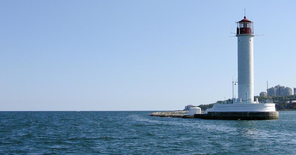 Blick aufs Meer, rechts ein Leuchtturm, im Hintergrund hohe Häuser.