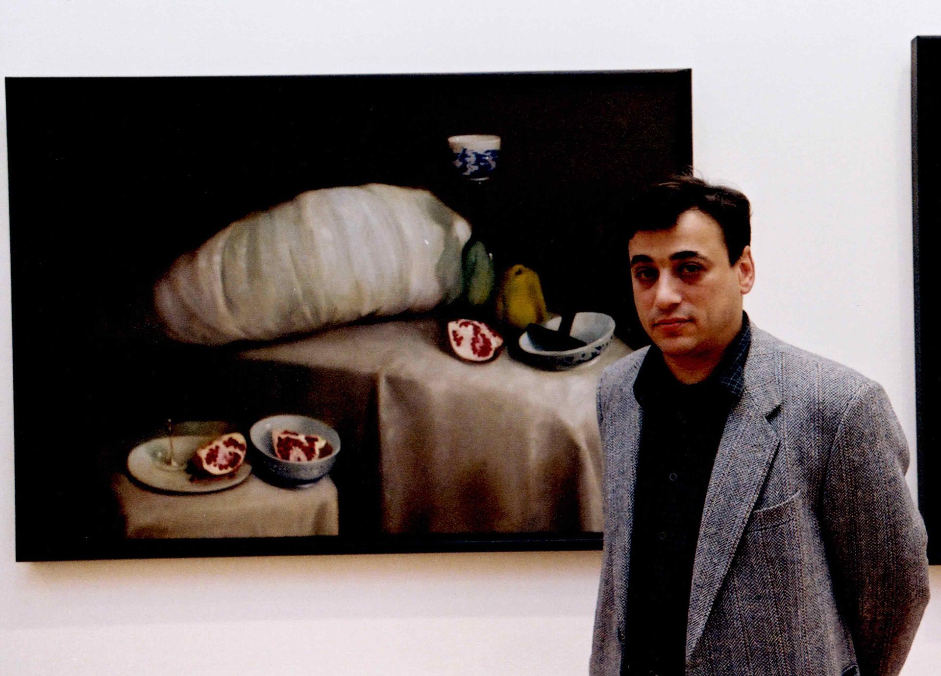 A young man stands in front of a still life depicting sliced pomegranates