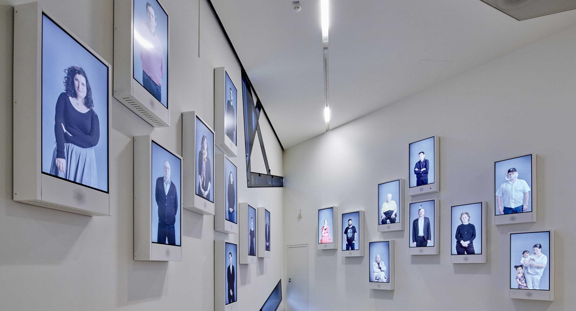 Room with several screens showing people looking friendly in to the camera.