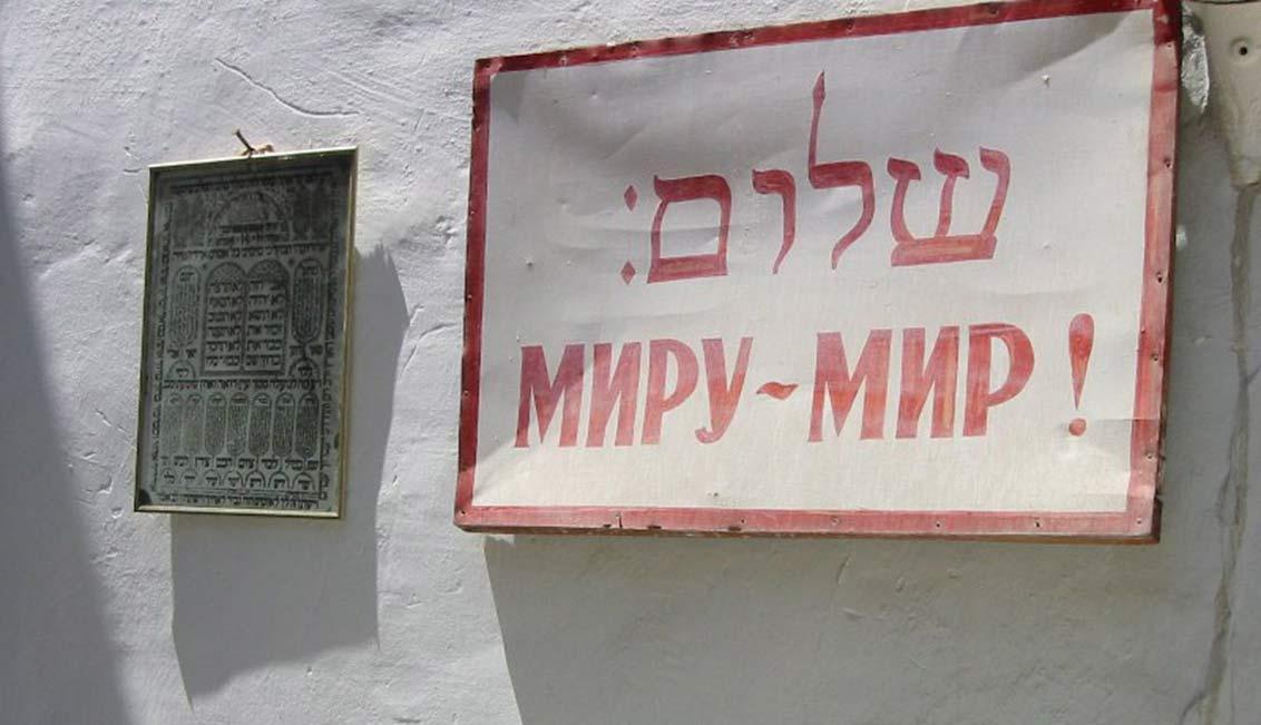 House wall with a sign that reads Shalom in Hebrew letters and Peace to the World in Russian