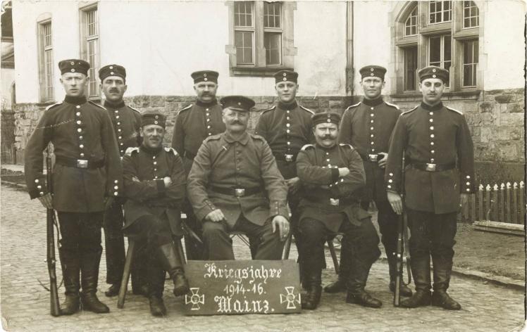 Black and white photo: Nine uniformed soldiers in front of barracks