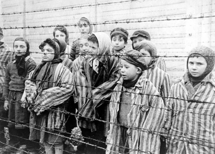 Black and white photograph with children in concentration camp clothes in Auschwitz standing behind barbed wire fence