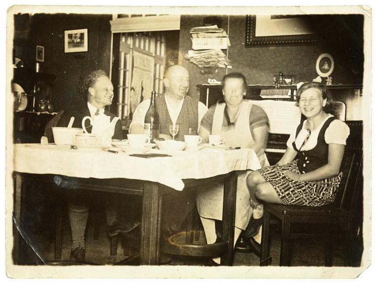  A black-and-white photo: four laughing people sitting at a dinner table set for a meal. Their faces are mostly blurred.