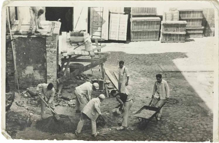Seven men in working clothes and with wheelbarrow, shovels and other equipment (black and white photo).