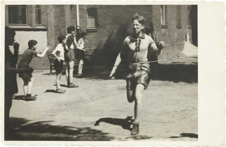 In the foreground of the picture you can see a running boy, who is about to reach the finish line, boys watching in the background (black and white photo).