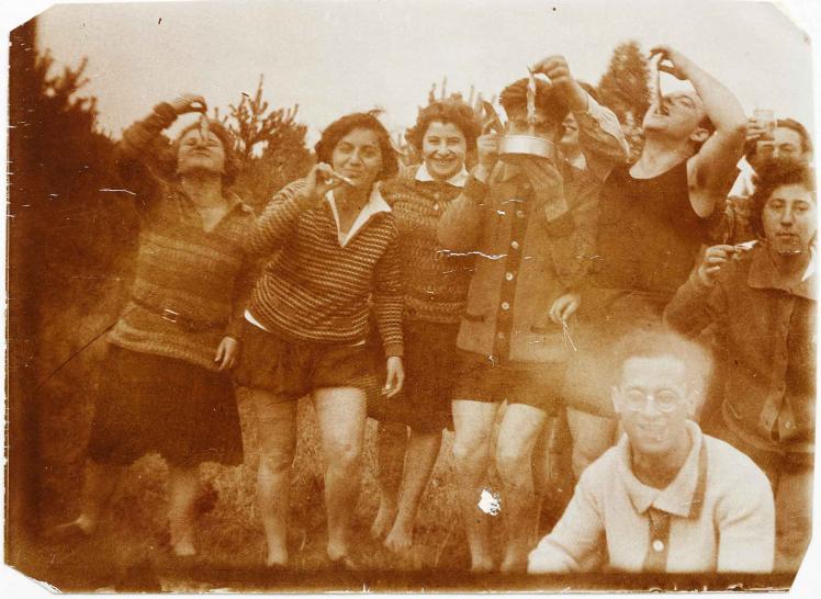 Gruppenbild von acht Frauen und Männern mit kurzen Hosen oder Röcken im Freien, die kleine Fische zum Mund führen