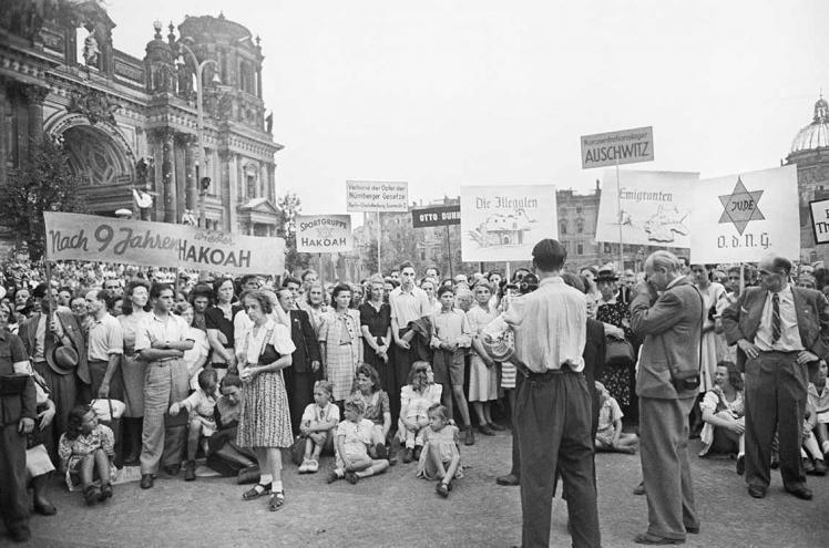 Black-and-white photograph: People holding signs in the air at a demonstration in front of the ruins of Berlin Cathedral.
