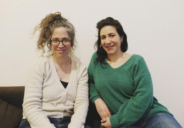 Two women sit next to each other and smile at the camera.