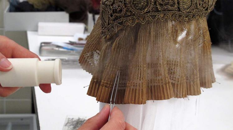 A hand uses a pair of tweezers to work on a bonnet