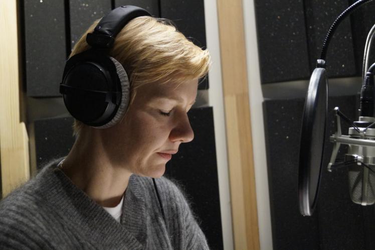 Actress and speaker Sandra Hüller sits with headphones in front of the microphone in the recording studio.